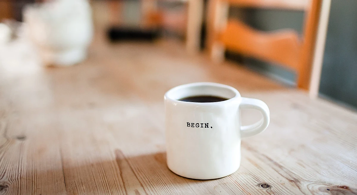 A full mug with the word "Begin" on it sits on a wooden table